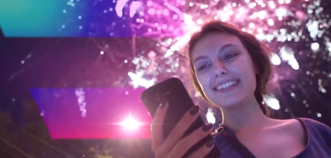 Eine Frau lächelt freudig auf ihr Smartphone, hinter ihr ist ein Feuerwerk zu sehen, links ist die Digital Austria-Fahne eingeblendet.