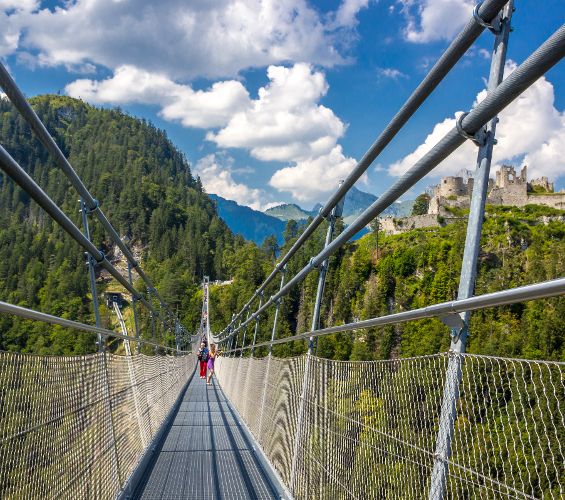 Zu sehen ist die Highline 179 Seilhängebrücke in Tirol an einem sonnigen Tag, eine Person überquert sie in weiter Ferne.